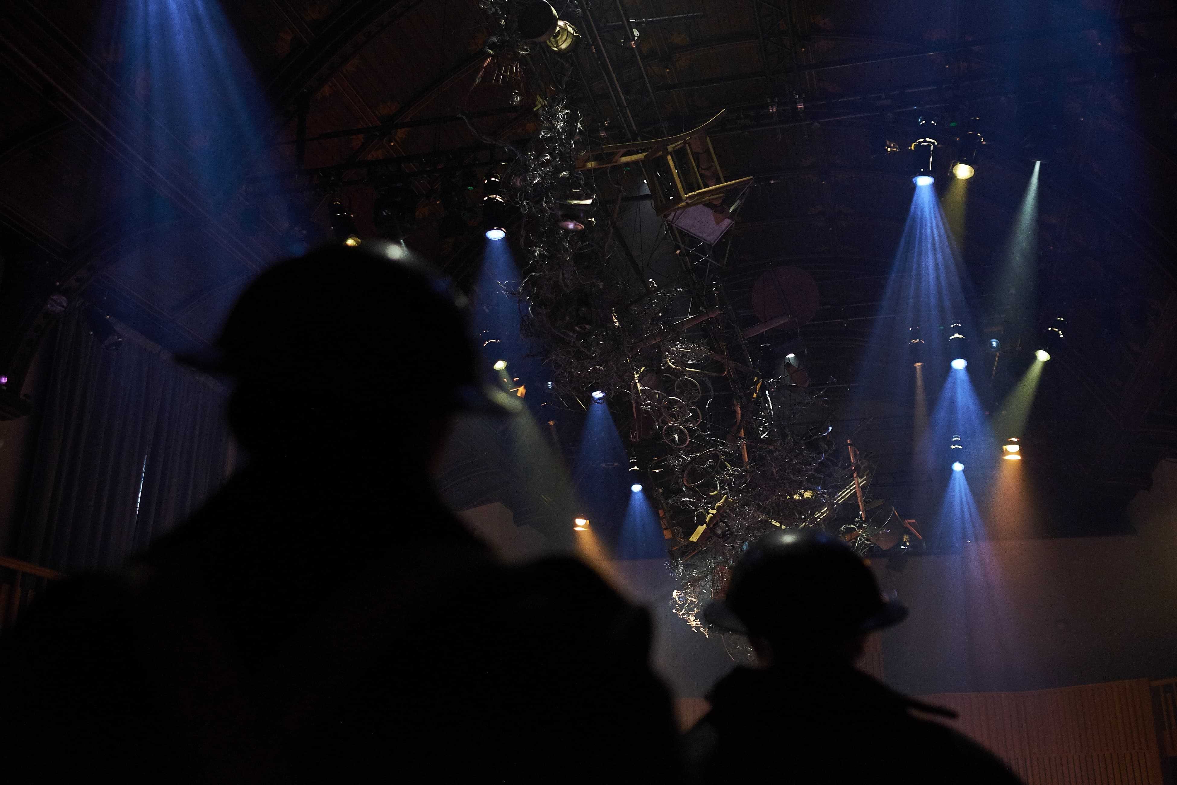 Silhouettes of two men in World War 1 helmets looking at rigging and lights on stage